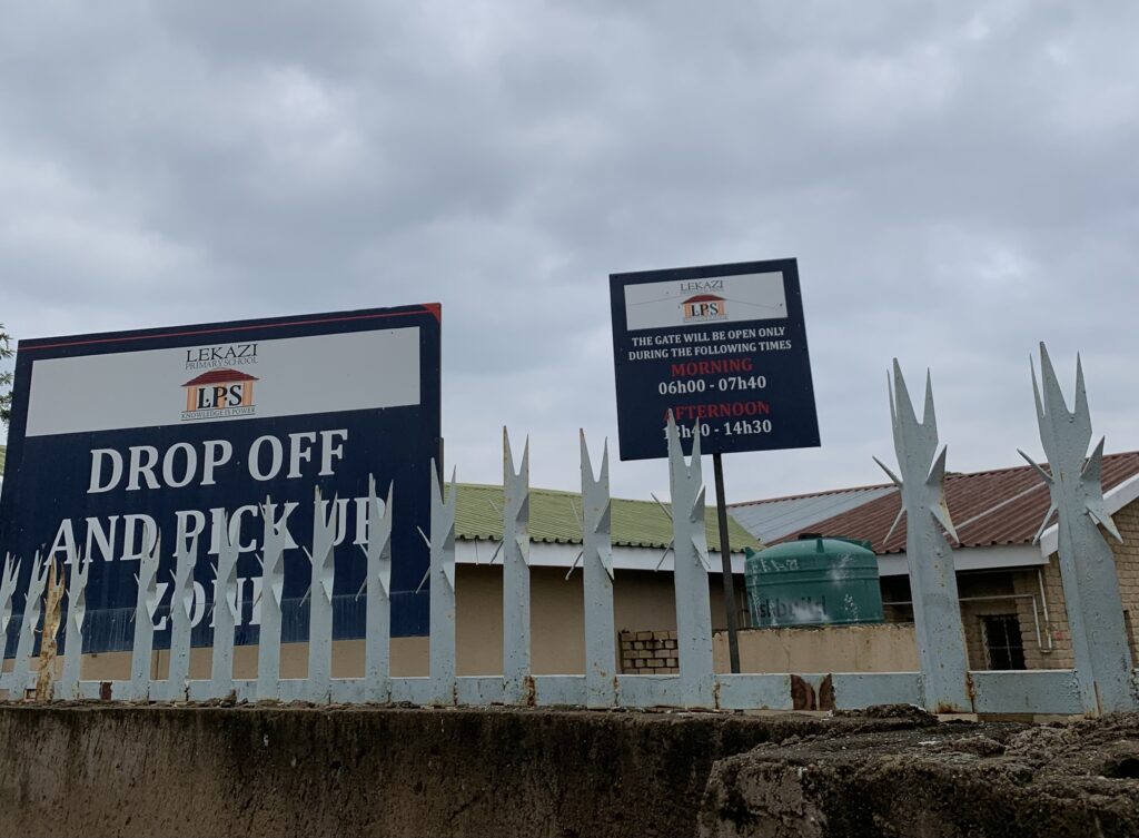 Lekazi Primary School entrance with drop-off and pick-up zone sign and gate opening times displayed
